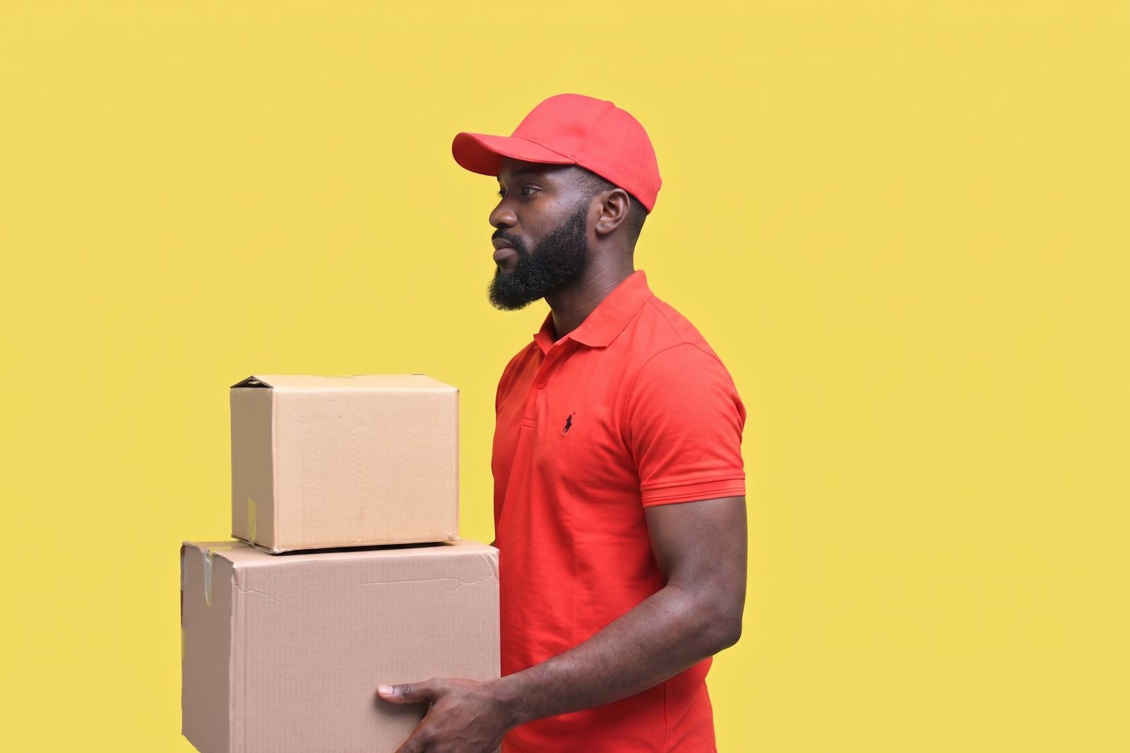 Un livreur en polo rouge portant deux cartons, sur fond jaune